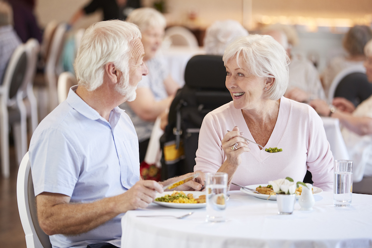 Senior Couple Eating Meal And Talking In Retirement Home